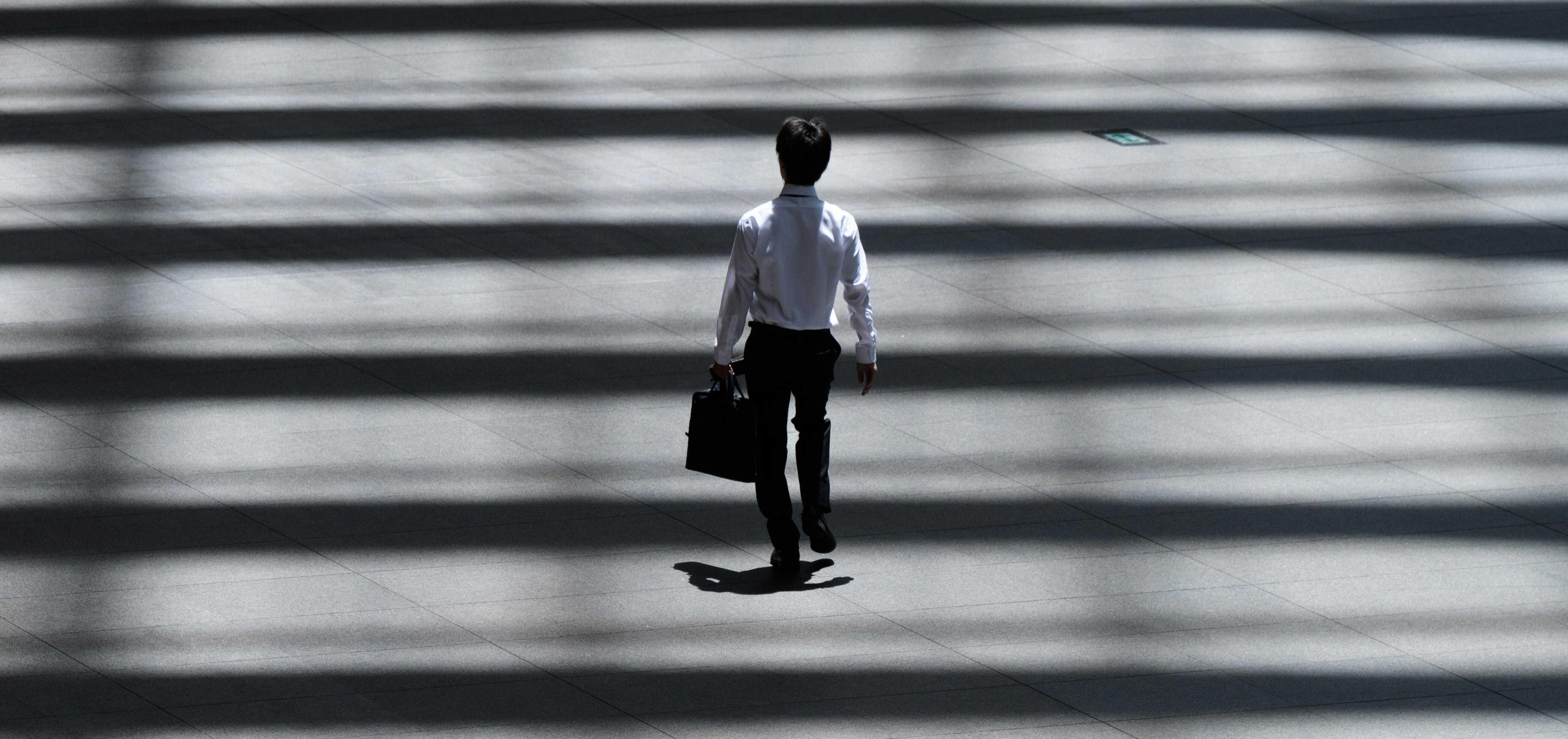 business man walking through the zebra walk made of lights and shadows. White shirt and black pants express the light and shadow.