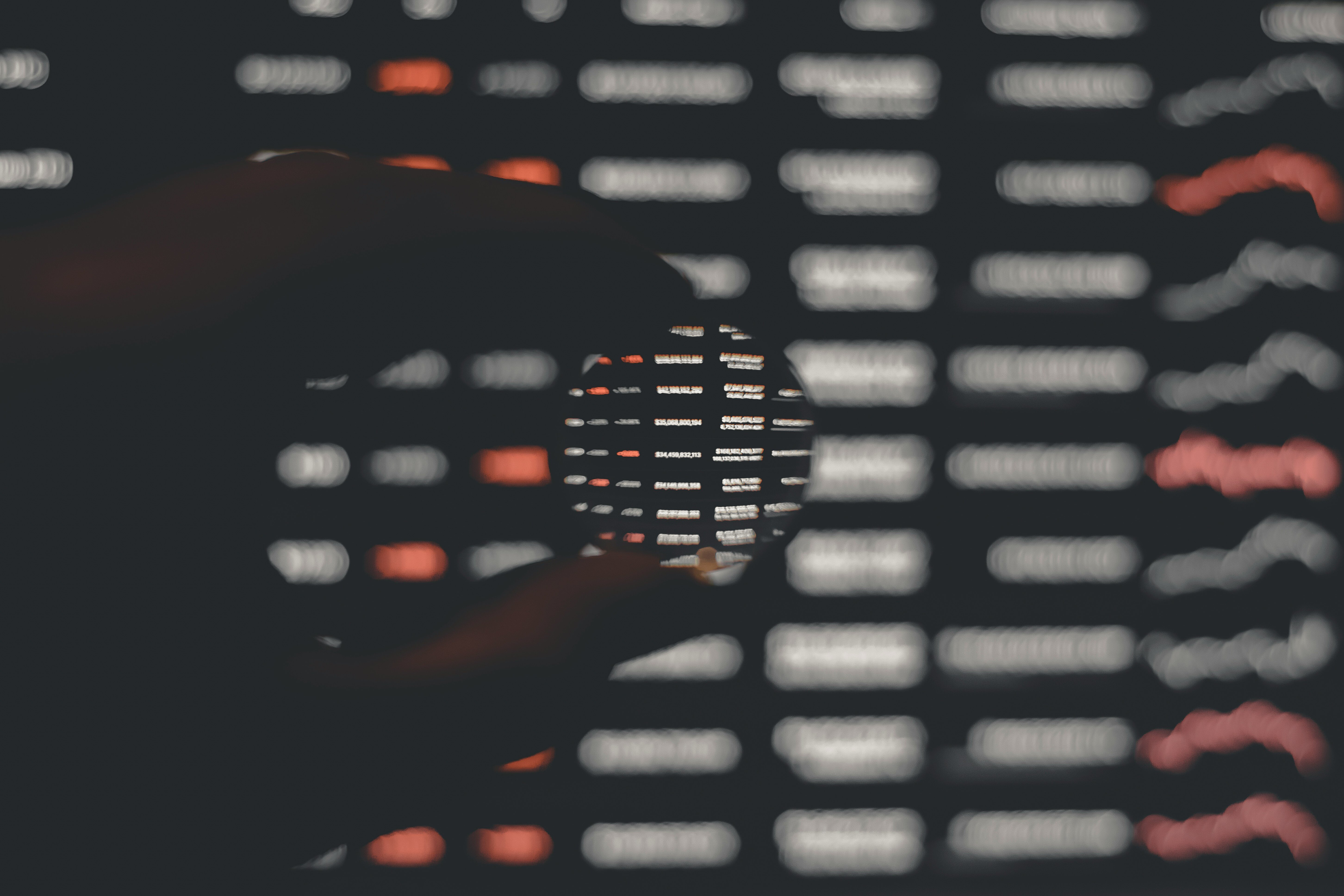 Close-up of a hand holding a magnifying glass focusing on blurred digital data on a screen, symbolizing data analysis and cybersecurity insights.